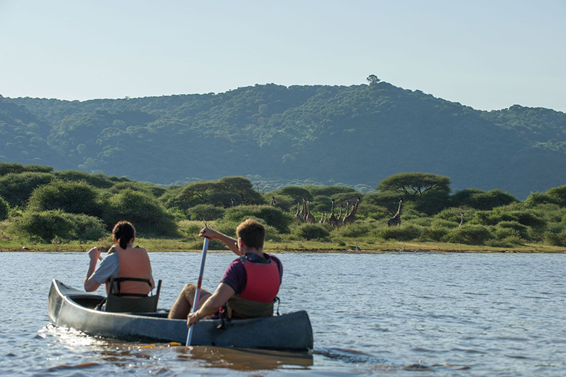 Canoë sur le lac Manyara avec des girafes et l'escarpement de Manyara en arrière-plan